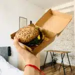 mana unei persoane tinand o cutie cu un buger d ela un fast food